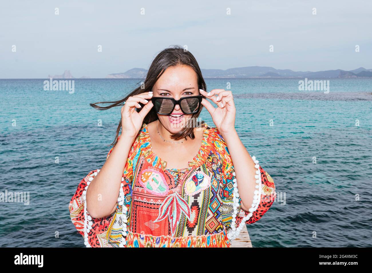Reife Frau in Sonnenbrillen mit offenem Mund, die vor dem Wasser auf Formentera Island steht Stockfoto