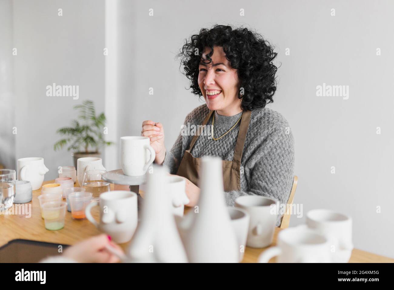 Fröhliche Künstlerin mit keramischen Produkten am Arbeitsplatz Stockfoto
