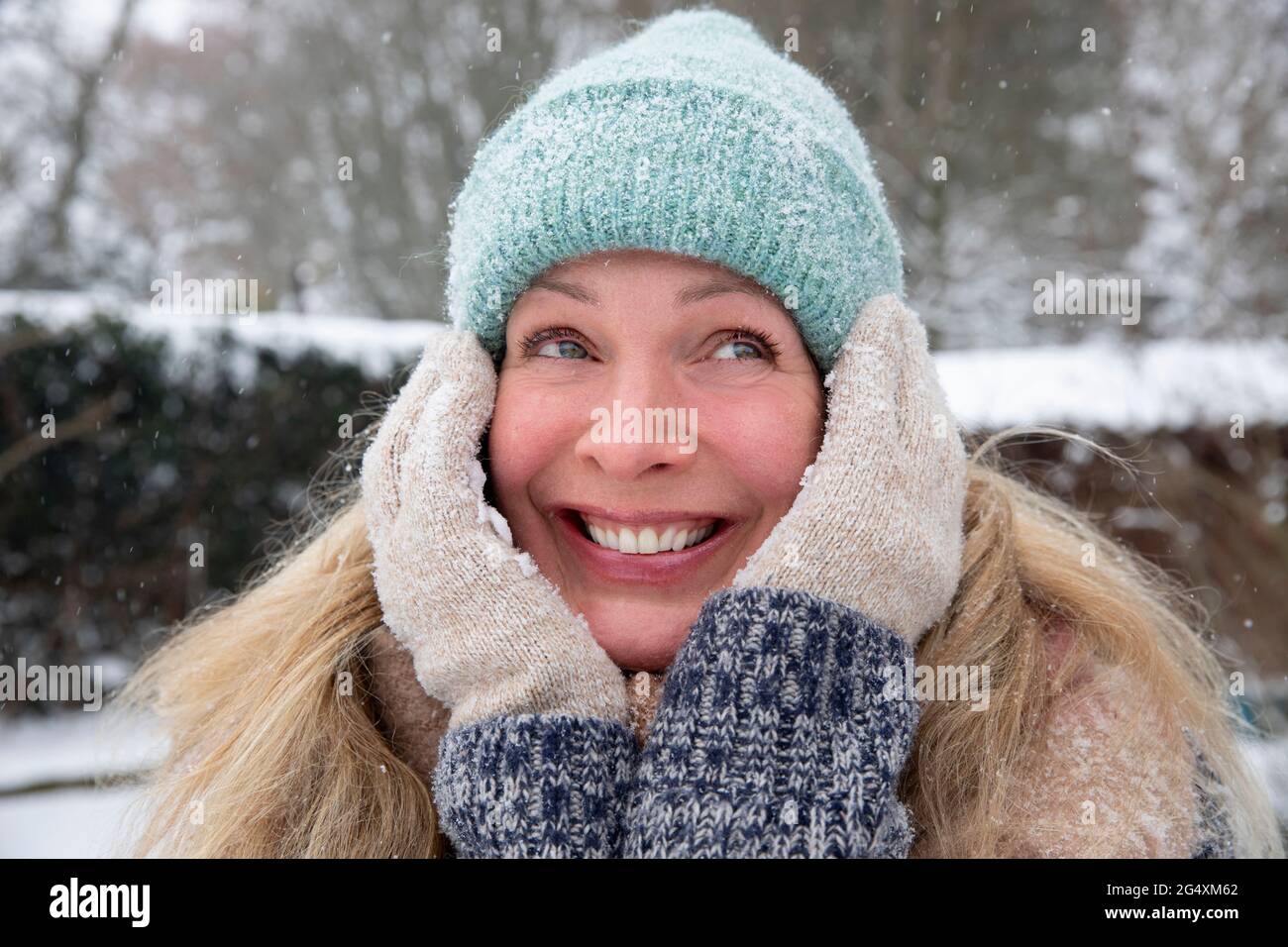 Glückliche blonde Frau, die im Winter mit der Hand auf dem Kinn im Hinterhof steht Stockfoto