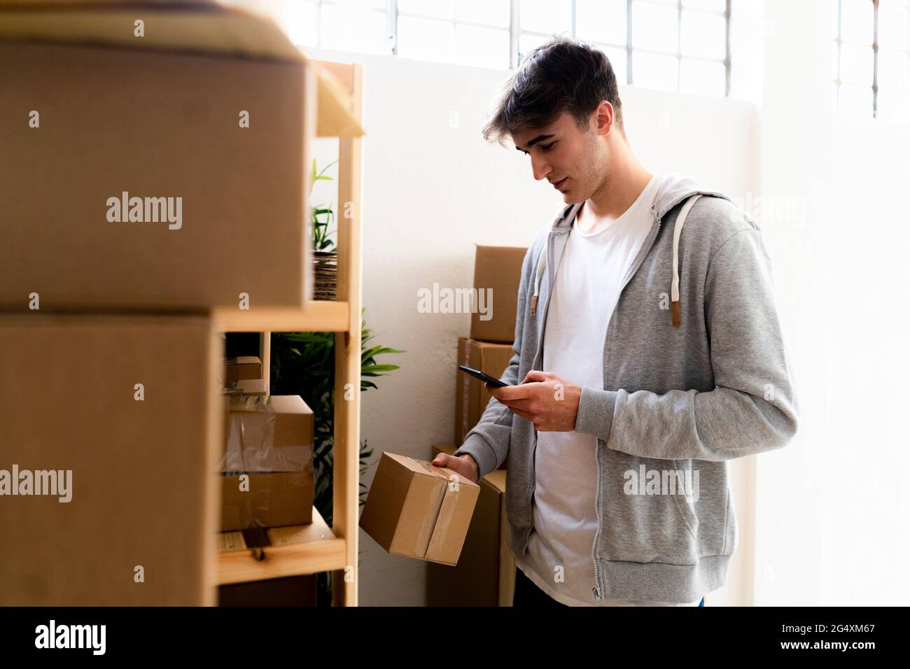 Geschäftsmann scannt Barcode auf der Box, während er vor dem Regal im Lager steht Stockfoto