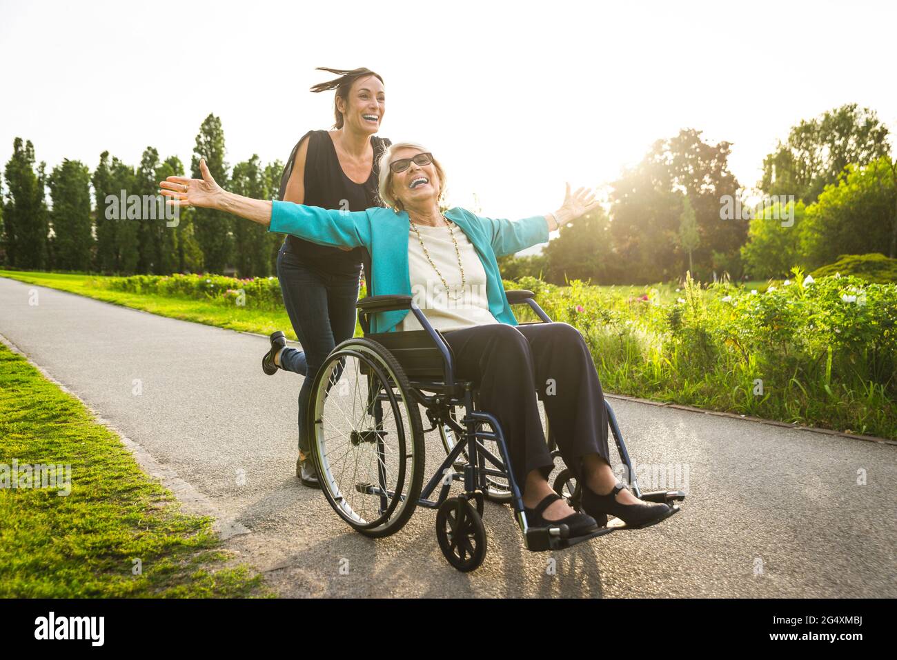 Glückliche Enkelin schiebt Großmutter im Rollstuhl im Park sitzen Stockfoto