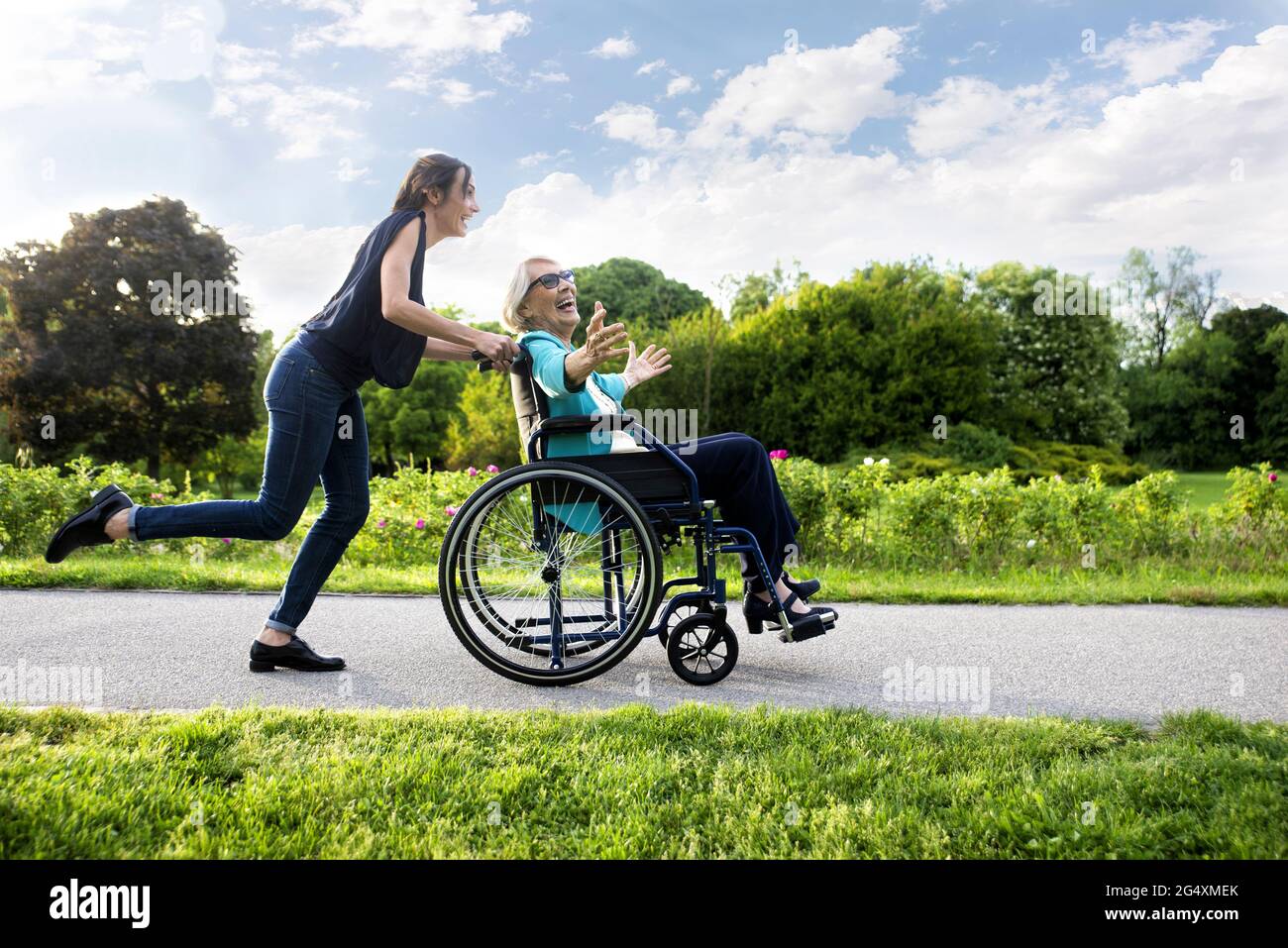 Glückliche Enkelin, die mit Großmutter im Rollstuhl im Park läuft Stockfoto
