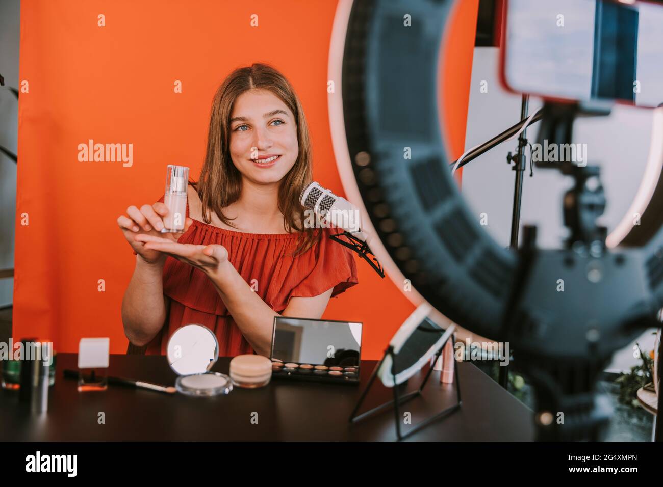 Lächelnde weibliche Influencerin präsentiert Foundation während der Dreharbeiten Make-up Tutorial zu Hause Workshop Stockfoto