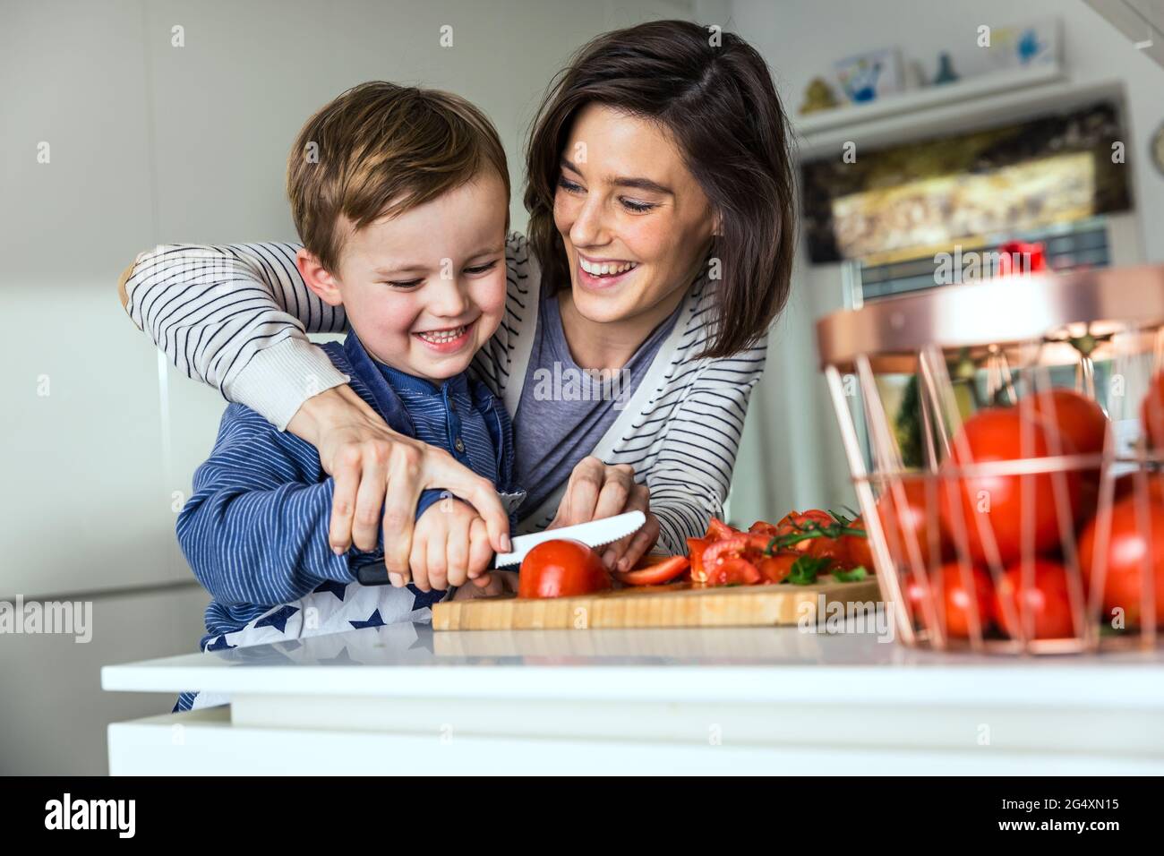 Mutter lehrt Sohn, Tomaten auf Schneidebrett in der Küche zu schneiden Stockfoto