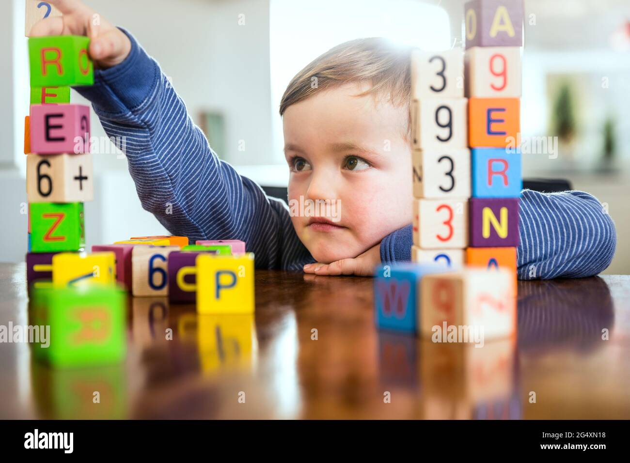 Netter Junge, der zu Hause mit Spielzeugblöcken auf dem Tisch spielt Stockfoto