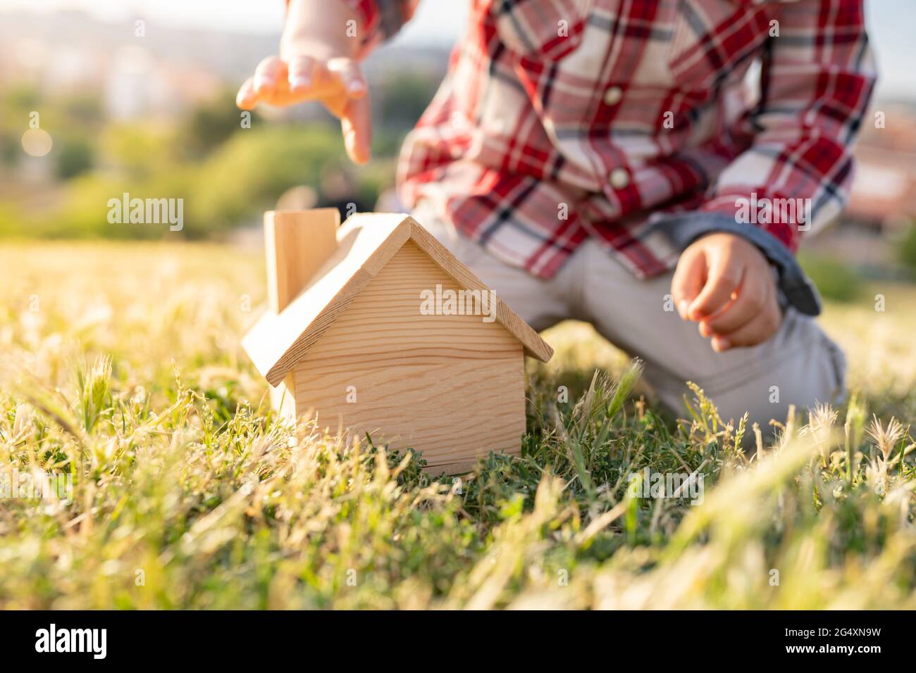 Junge spielt mit Holzhausspielzeug auf Gras an sonnigen Tagen Stockfoto