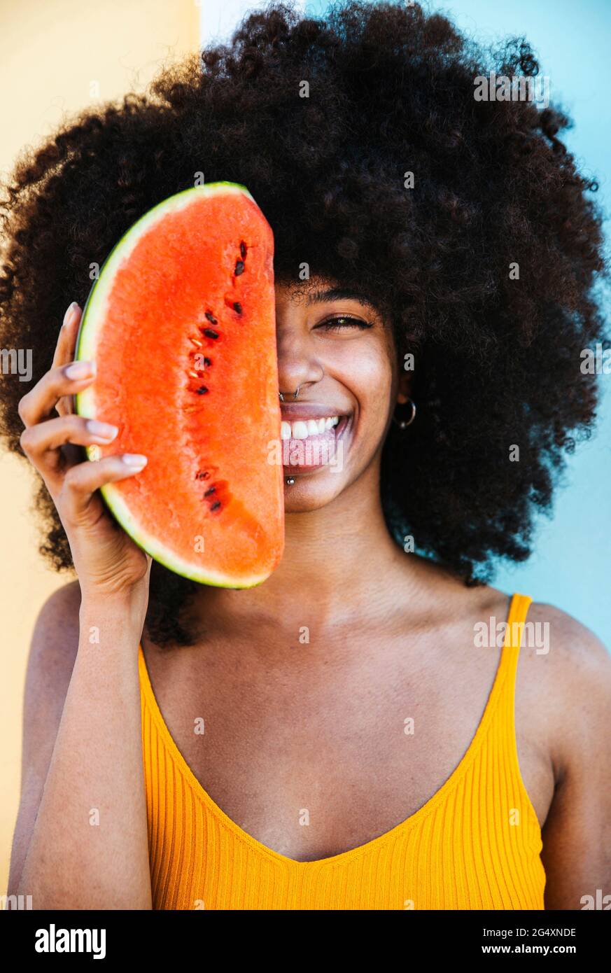 Verspielte junge Frau mit Wassermelonenscheibe vor dem Gesicht Stockfoto