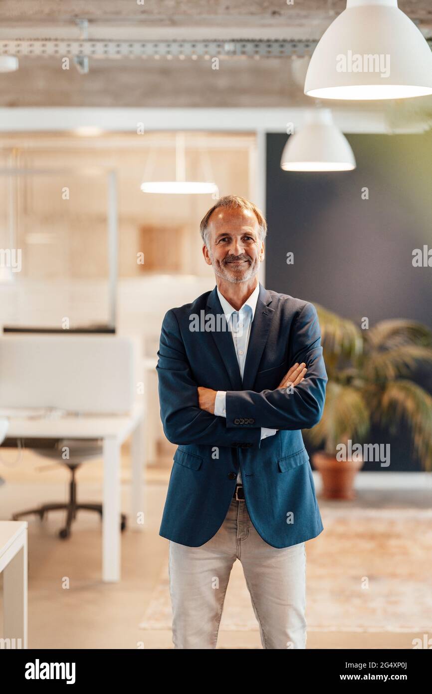Leitender männlicher Unternehmer, der im Amt mit gekreuzten Armen steht Stockfoto
