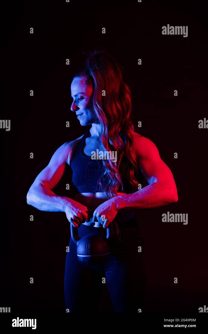 Muskulöse Frau mit Kugelhantel auf schwarzem Hintergrund Stockfoto
