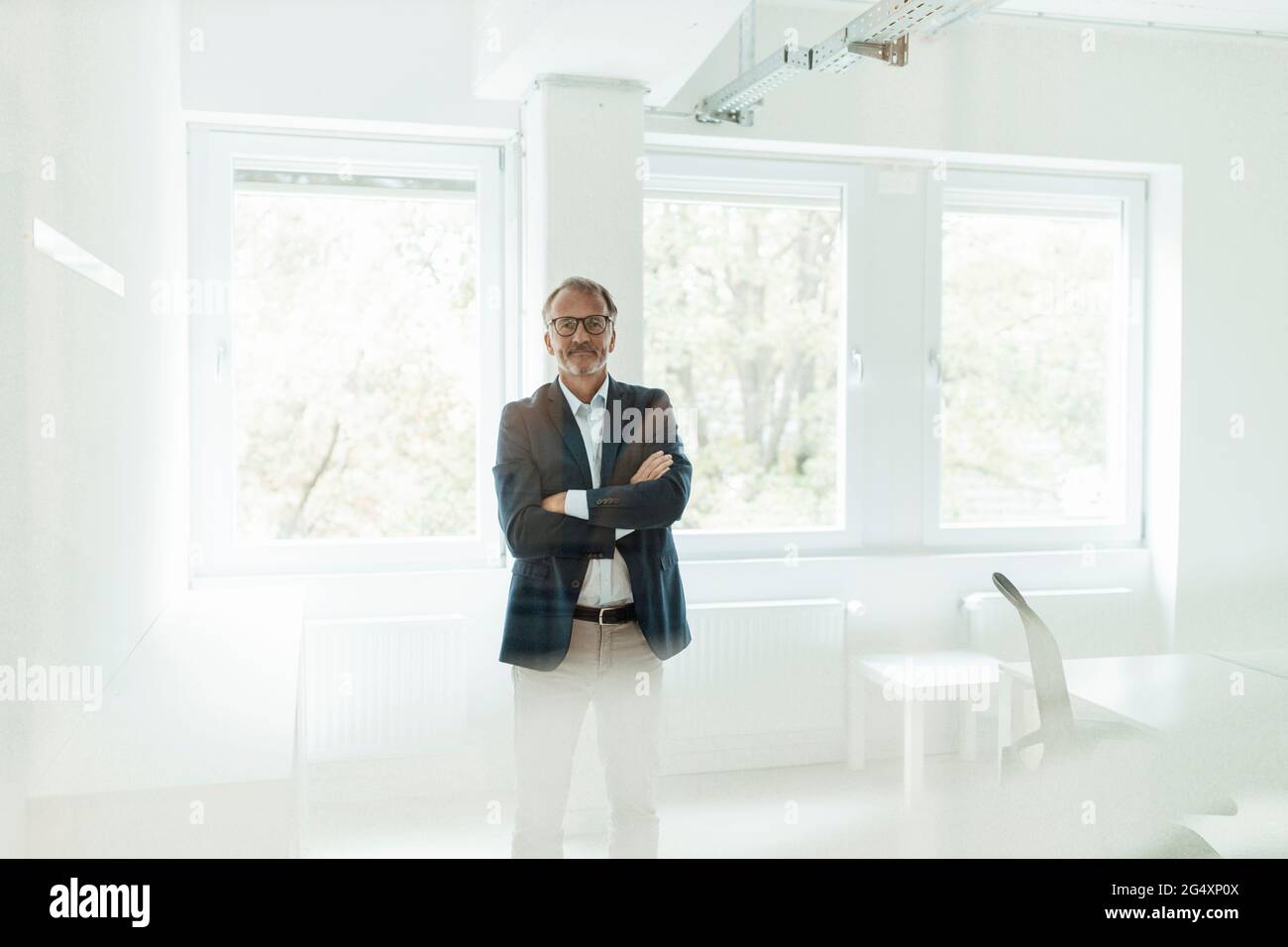 Leitender männlicher Unternehmer mit gekreuzten Armen, die im Büro stehen Stockfoto