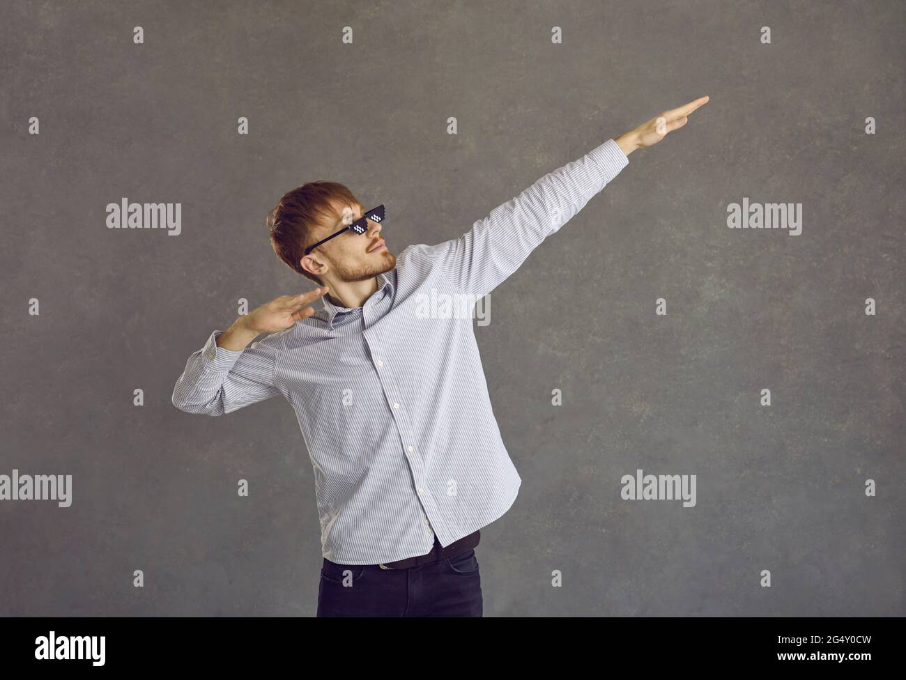 Junger Geschäftsmann in einer zermetzten Lebensbrille, die vor grauem Studiohintergrund tänzelte Stockfoto