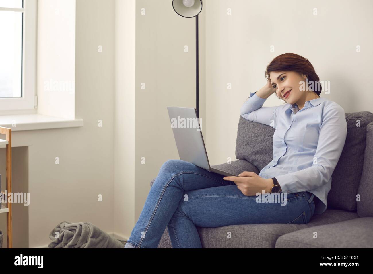 Lächelnde Millennials-Frau, die auf den Laptop-Bildschirm schaut, entspannen Sie sich auf der Couch zu Hause Stockfoto
