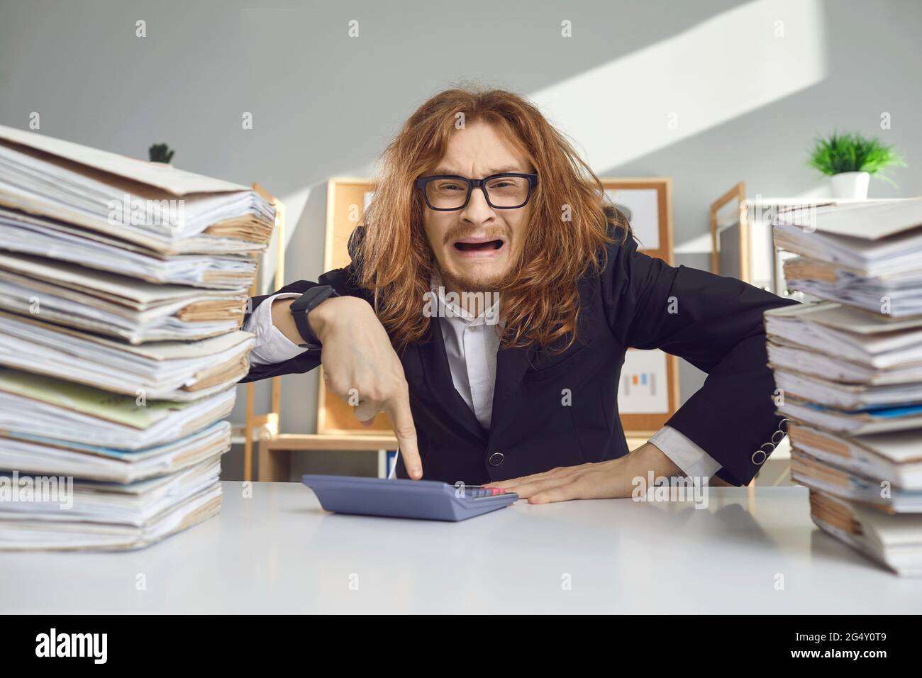 Verrückter männlicher Buchhalter sitzt zwischen den Dokumenten und drückt nervös Tasten auf dem Rechner. Stockfoto