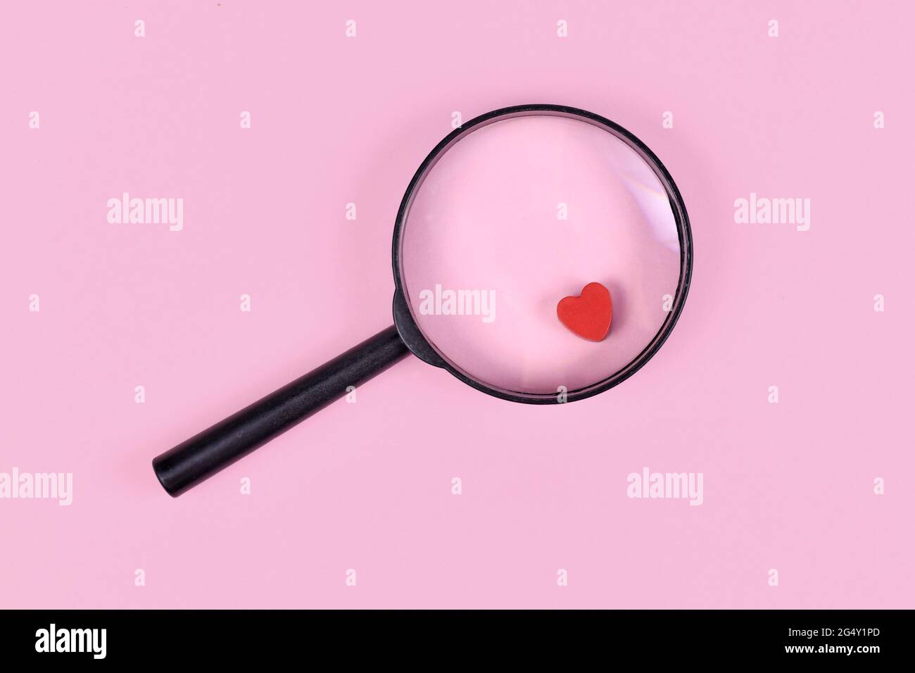 Konzept zur Liebesfindung mit Lupenglas und rotem Herz-Symbol auf rosa Hintergrund Stockfoto