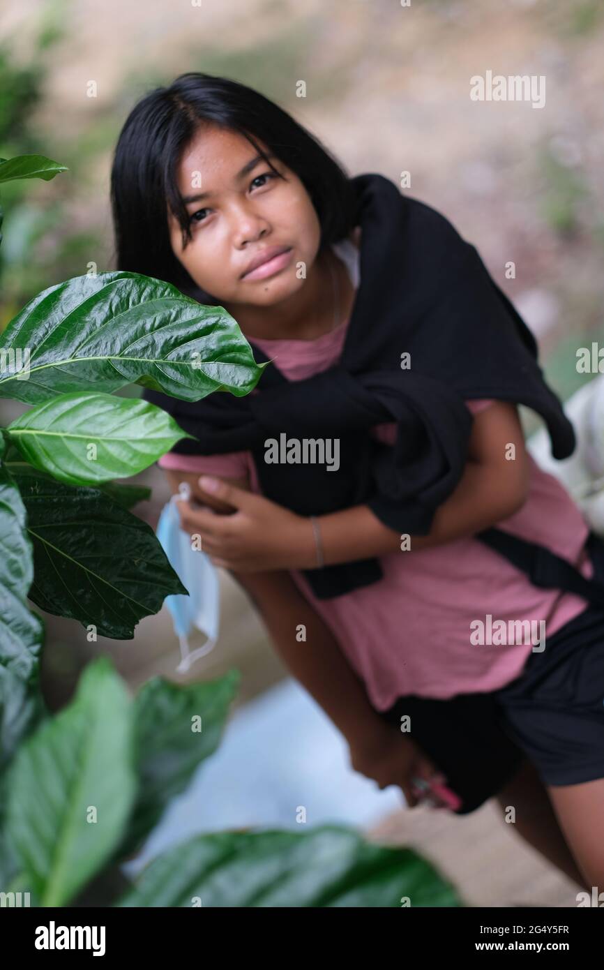 Ein Teenager-Thai-Mädchen schaut nach unten, zum Teil mit einem Blatt tropischer Bäume bedeckt Stockfoto