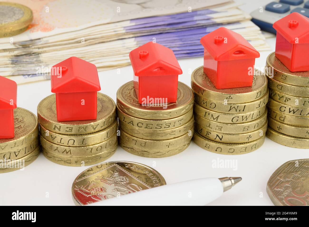 Steigende Stapel von Münzen mit Spielzeughäusern auf der Oberseite, um einen steigenden Immobilienmarkt darzustellen. Stockfoto