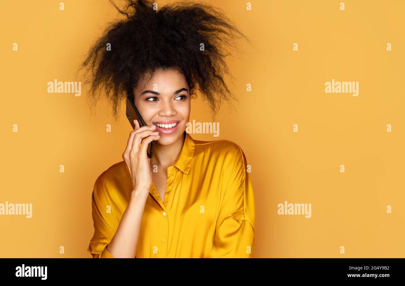 Mädchen spricht am Telefon und lächelt. Foto von afroamerikanischen Mädchen auf gelbem Hintergrund Stockfoto