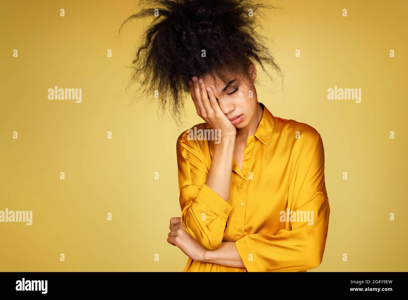 Müde Mädchen bedeckt Gesicht mit Handfläche, fühlt sich überfordert und Müdigkeit. Foto von afroamerikanischen Mädchen auf gelbem Hintergrund Stockfoto