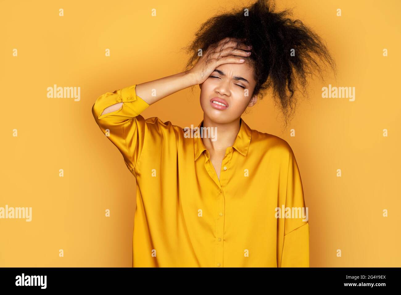 Müde Mädchen hält die Hand auf der Stirn gedrückt, deprimiert. Foto von afroamerikanischen Mädchen auf gelbem Hintergrund Stockfoto