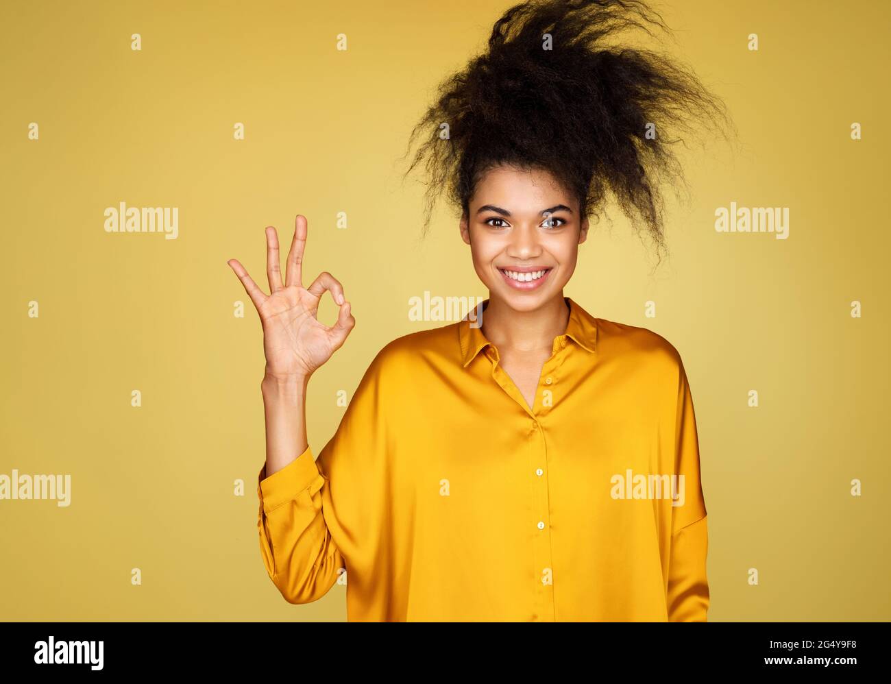 Junges Mädchen sagt gute Arbeit oder gut gemacht, macht okay Geste. Foto von afroamerikanischen Mädchen auf gelbem Hintergrund Stockfoto