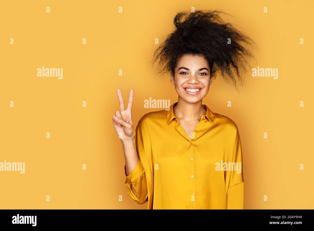 Lächelndes Mädchen, das ein Friedenszeichen oder eine V-Geste mit den Fingern zeigt. Foto von afroamerikanischen Mädchen auf gelbem Hintergrund Stockfoto