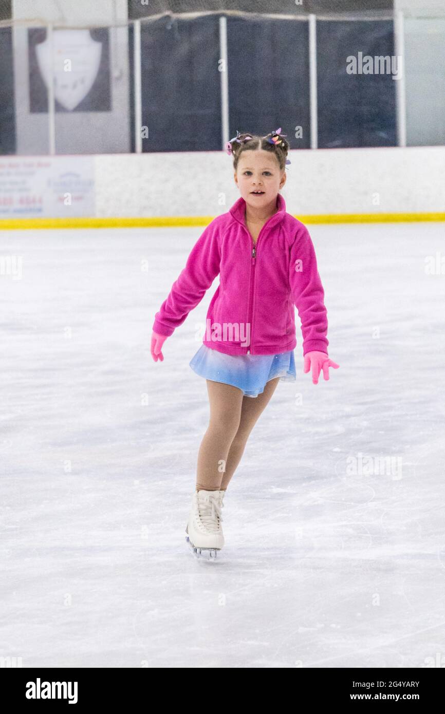 Kleines Mädchen, das Eiskunstlauf auf einer Indoor-Eisbahn übt. Stockfoto