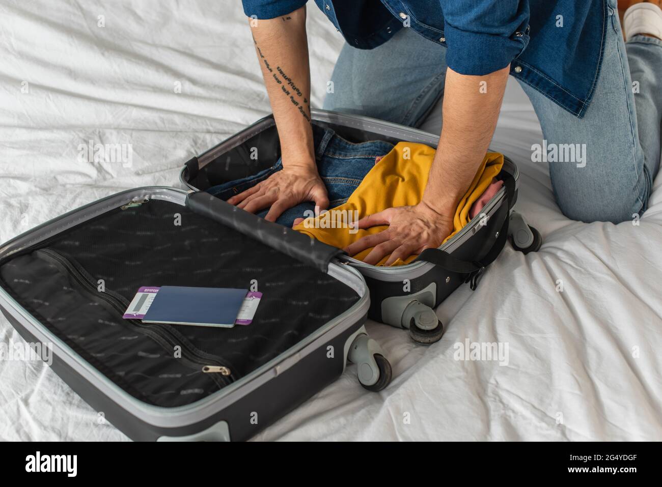 Verkürzte Ansicht von Touristen, die Kleidung im Koffer neben dem Pass pressen, mit Bordkarte auf dem Bett Stockfoto