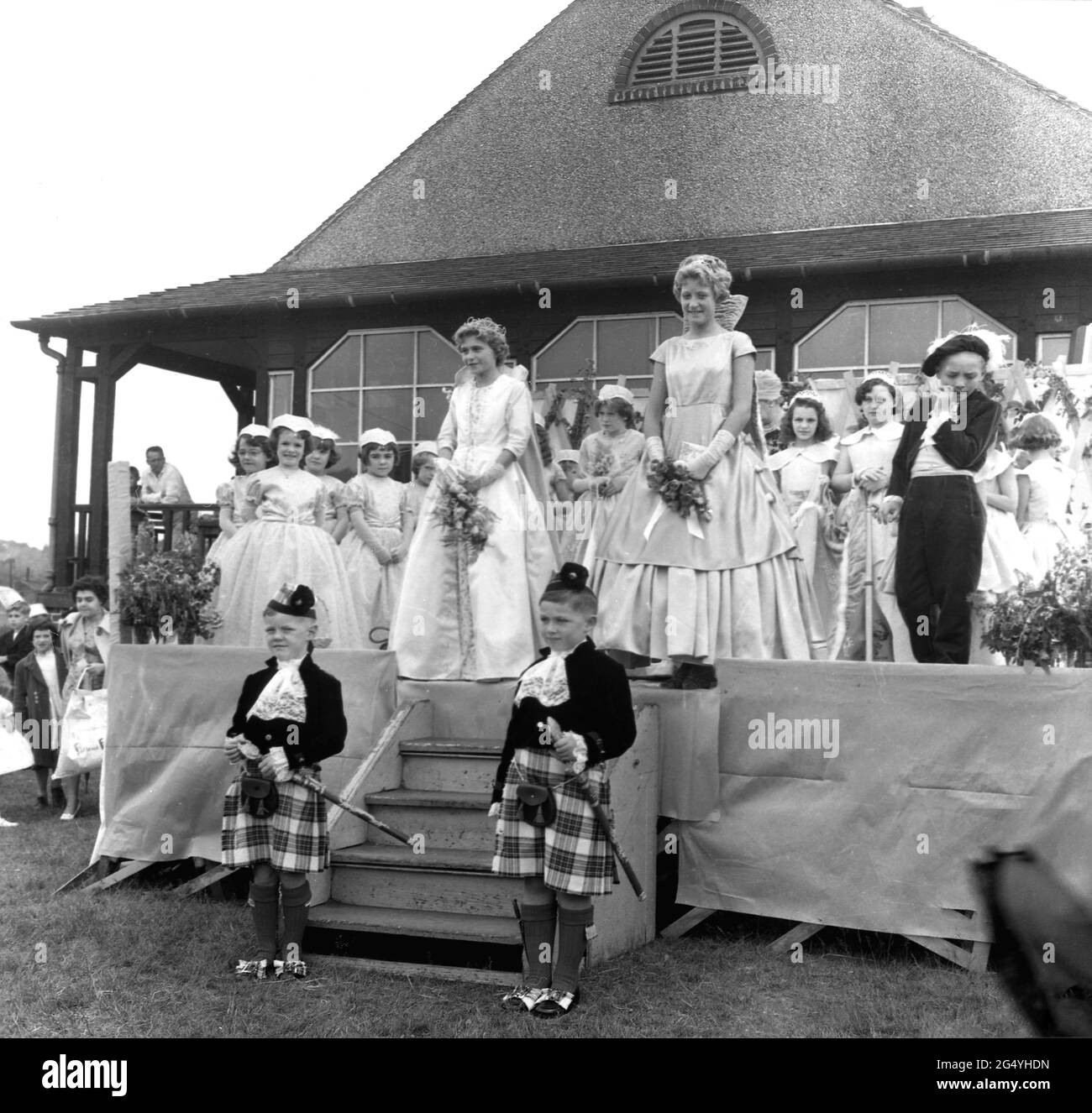 1950s, historisch, in einem öffentlichen Park, wurde ein Mädchen auf einer temporären Bühne zur Rose Queen', Farnworth, Lancashire, England, Großbritannien, gekrönt. Ab dem Jahr 1880s wurde das Rose Queen Festival, das im Juni stattfand, zu einem jährlichen Ereignis in Städten und Dörfern in ganz Großbritannien, insbesondere in Lancashire, der Grafschaft, die nach den Rosekriegen (1455-87) als Rotrose County bekannt ist. Das Rosenkönigin-Fest war ähnlich wie das Maifest, das den Beginn des Sommers markierte. Stockfoto