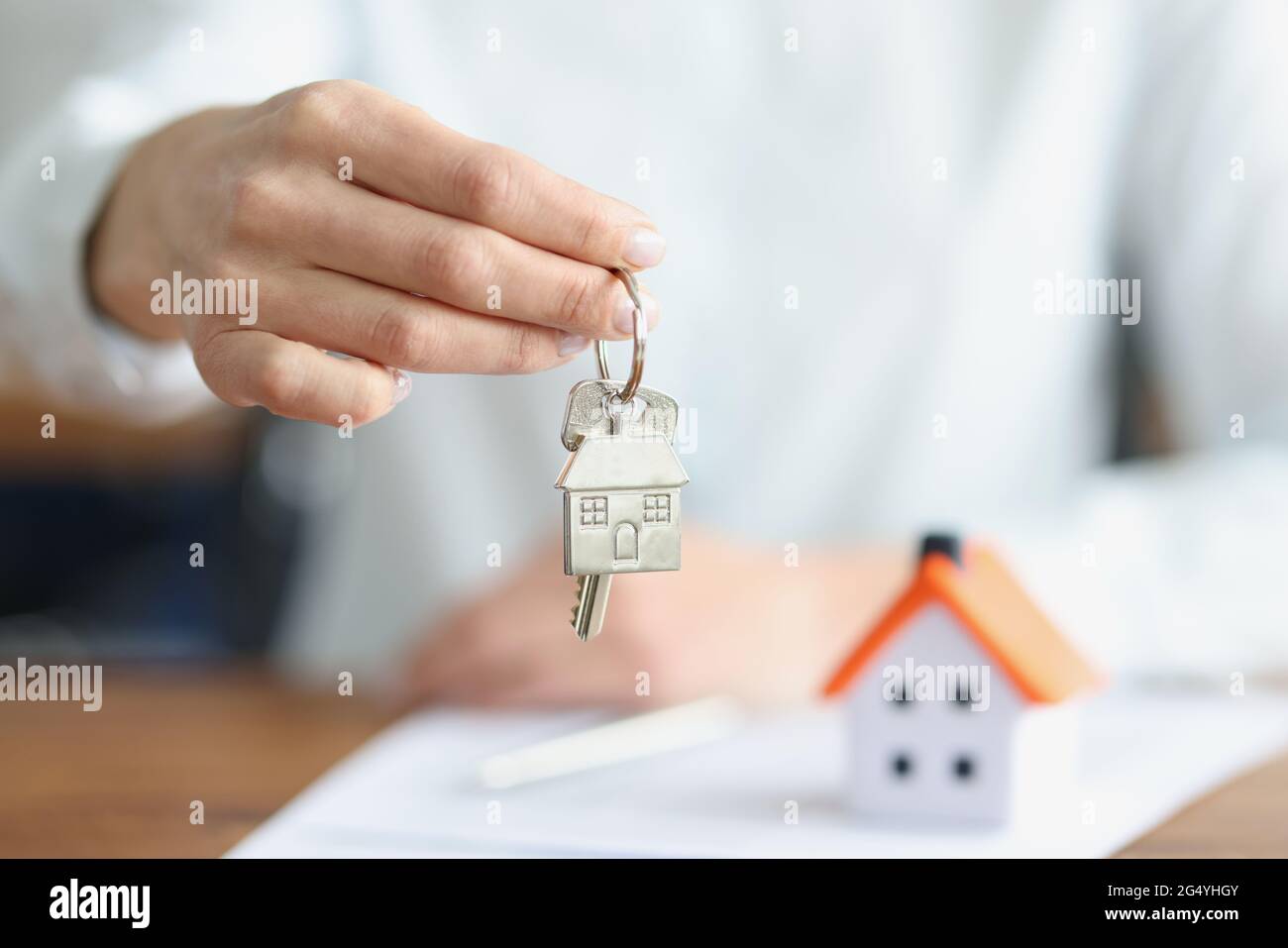 Weibliche Hand, die Schlüssel mit Schlüsselanhänger in der Nähe des Spielzeughauses hält Stockfoto