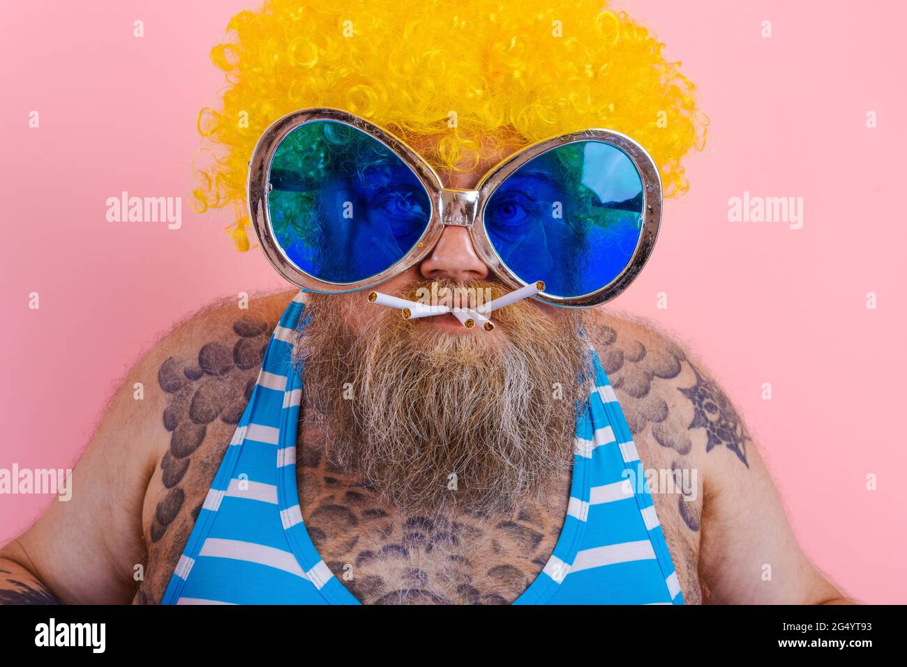 Fetter, ernsthafter Mann mit Bart und Perücke raucht Zigaretten Stockfoto