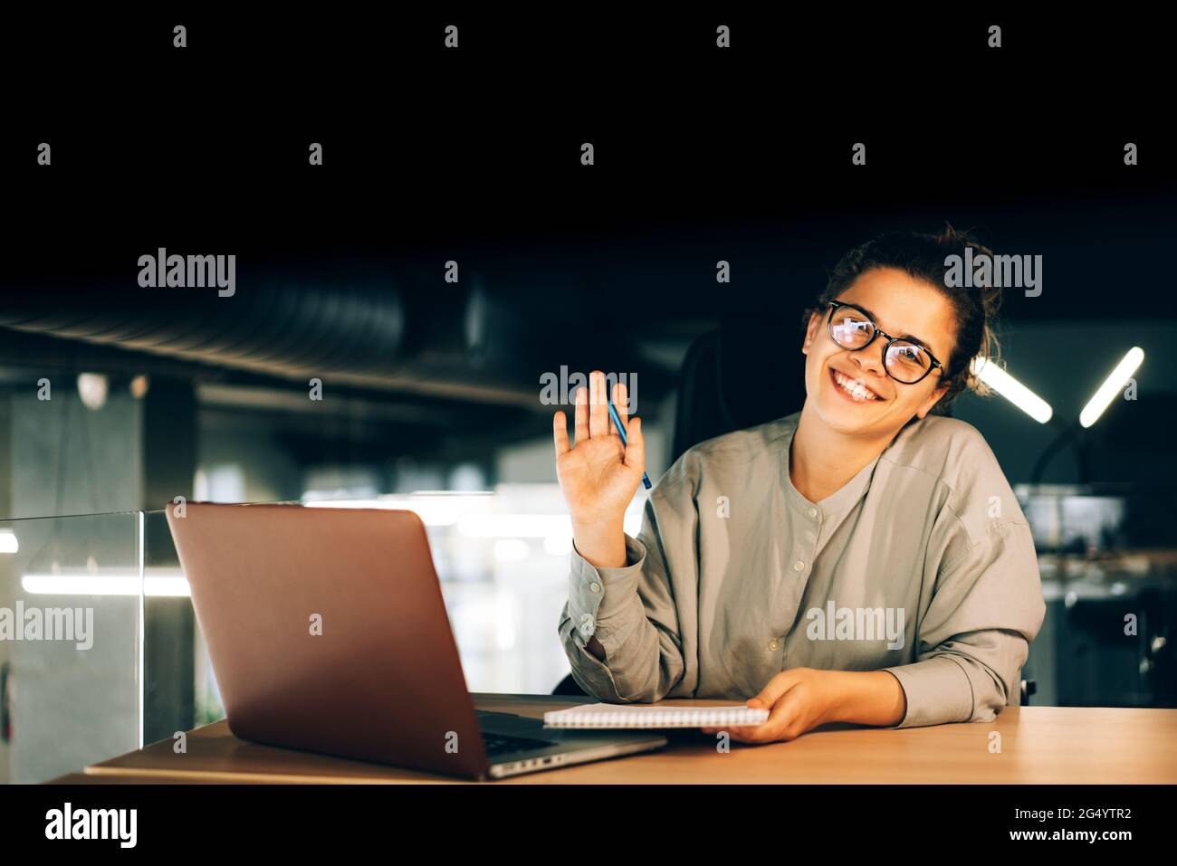 Geschäftsfrau mit Brille im Büro, beim Arbeiten oder Studieren mit dem Laptop und Notizblock. Isolierter schwarzer Hintergrund für einfaches Design. Stockfoto