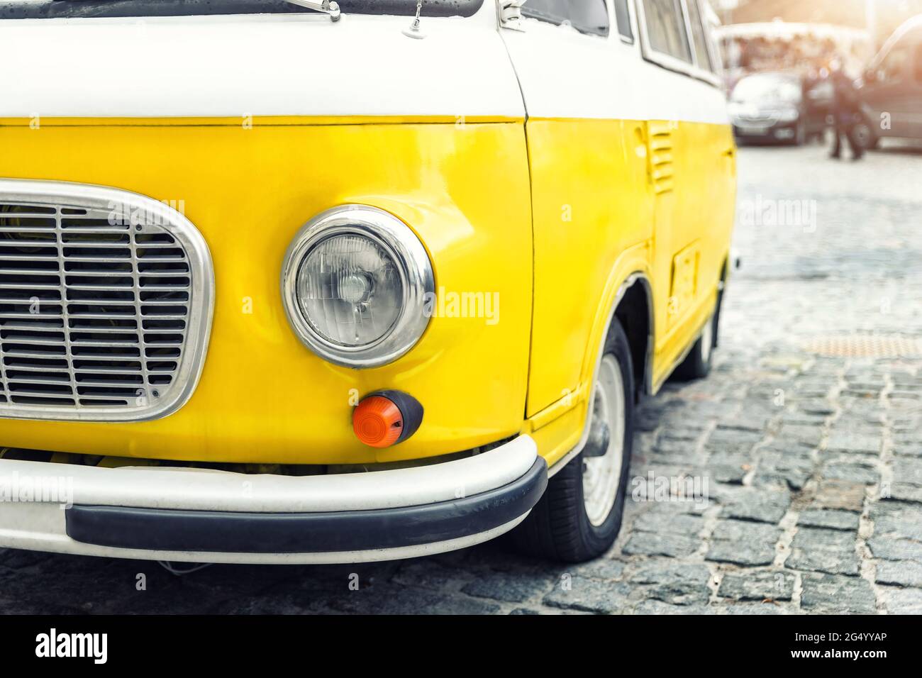 Nahaufnahme Detail Vorderansicht des Scheinwerferteils alten Vintage leuchtend gelben Retro-Minibus Auto van geparkt in der europäischen Innenstadt auf Kopfsteinpflaster gepflastert Stockfoto