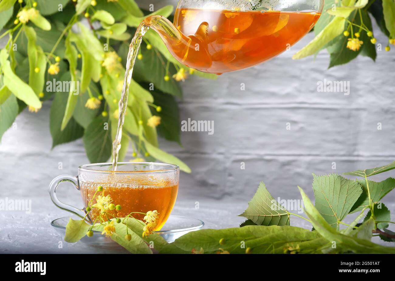 Frisch gebrühter Limetttee wird vor dem Hintergrund einer Ziegelwand in eine Tasse Teekannen gegossen Stockfoto
