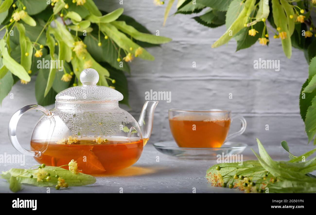 Vor dem Hintergrund einer Ziegelwand, eine Teekannen und eine Tasse mit Lindentee und Blumen auf einem Holztisch Stockfoto