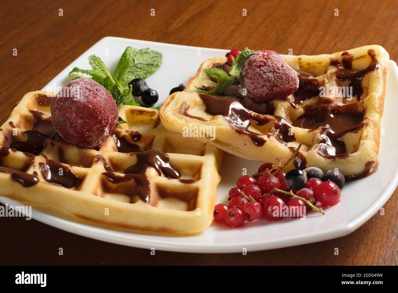 Zwei große Waffeln mit Schokolade, gefrorenen Erdbeeren und Beeren auf einem weißen Teller Stockfoto