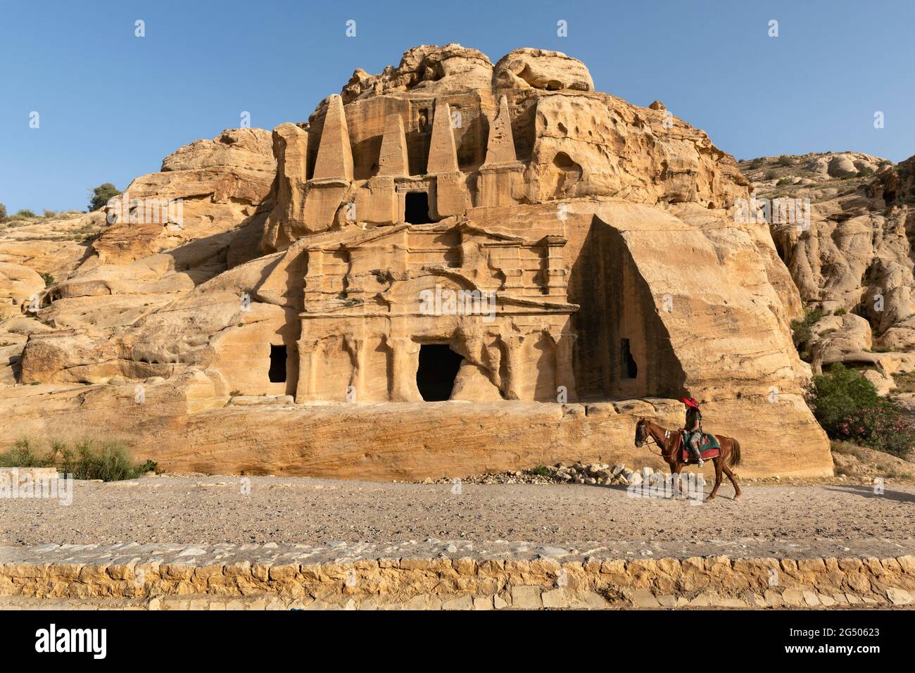 Touristenüberquerung des Obelisken-Grabes und des Bab Al-Siq Triclinium zwischen dem Petra Besucherzentrum und dem Eingang zum Siq. Stockfoto