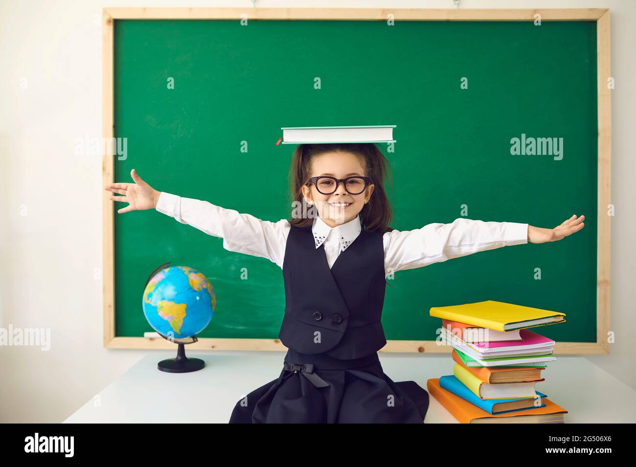Zurück zum Schulkonzept. Schulmädchen mit Brille lächelt im Klassenzimmer mit einer Schultafel. Stockfoto