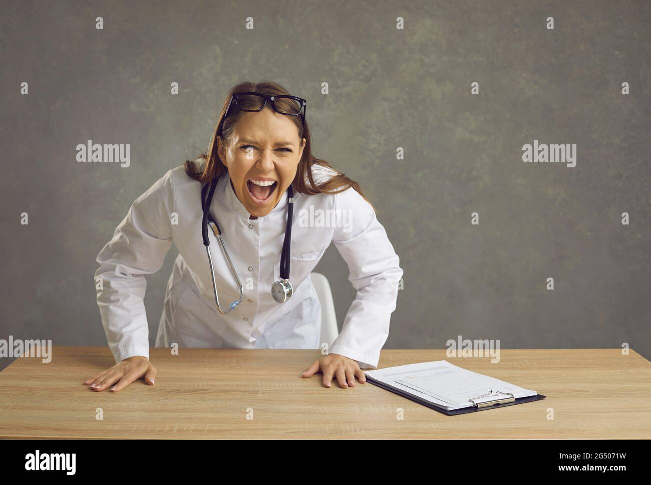Wütend wütende Ärztin schreiend auf Kamera hinter Schreibtisch Studio Schuss stehen Stockfoto
