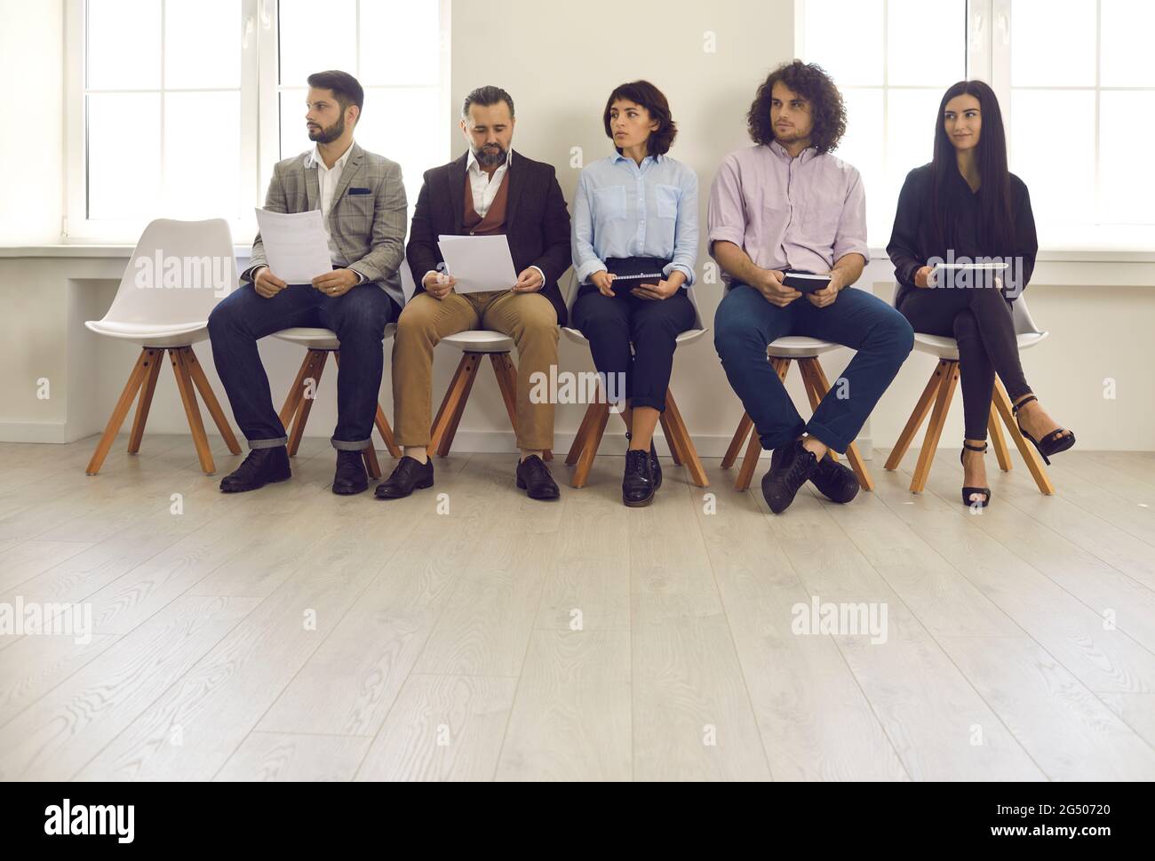 Kandidaten mit Lebensläufen in den Händen sitzen auf Stühlen in der Lobby und warten auf ein Interview. Stockfoto