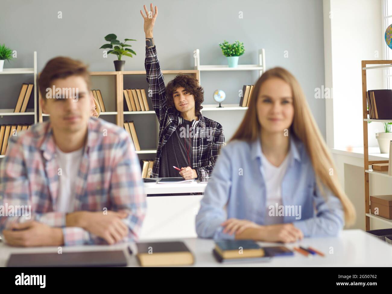 Gymnasiast, der am Schreibtisch sitzt und die Hand hebt, um im Unterricht Fragen zu beantworten oder zu stellen Stockfoto