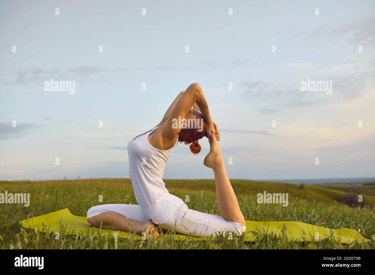 Fit Frau in aktive unterwegs dabei eine beinige King Pigeon Pose ruht auf Yoga-Matte im grünen Feld Stockfoto