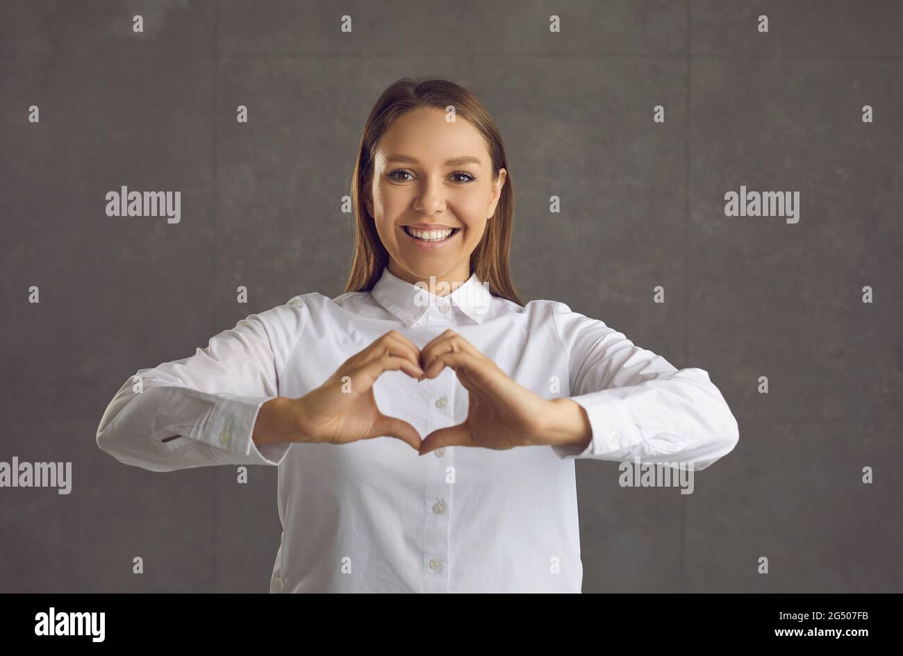 Porträt einer schönen weiblichen Model macht eine Herzgeste auf einem grauen Hintergrund. Stockfoto