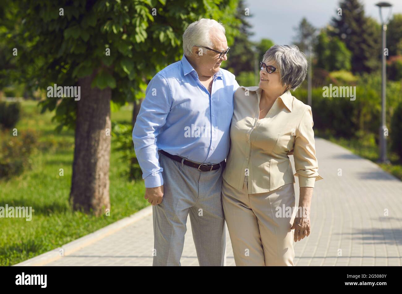 Porträt eines glücklichen Seniorenpaares, das an einem sonnigen Sommertag in einem grünen Park spazieren geht Stockfoto