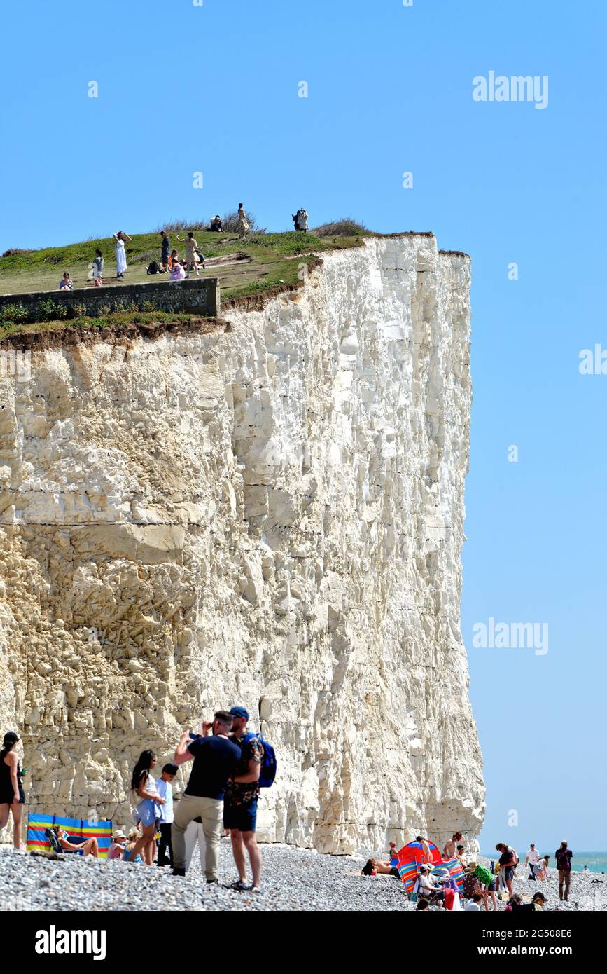 Die instabilen Kreidefelsen von Birling Gap, die an einem heißen Sommertag vom Strand aus mit Menschen am Rand der Klippen Eastbourne East Sussex England betrachtet werden Stockfoto