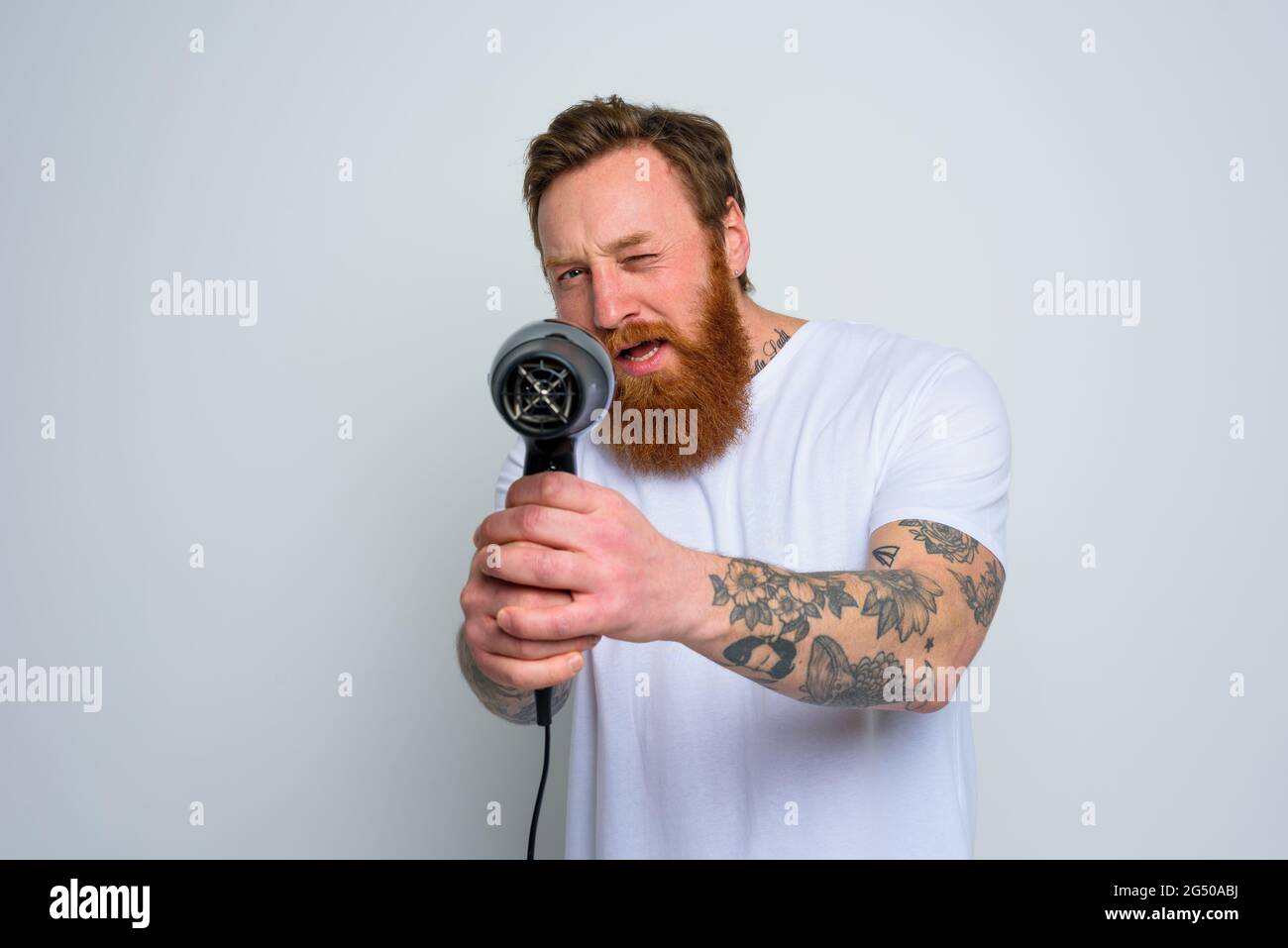 Serious Mann mit Bart spielen mit Haar dryeras eine Pistole Stockfoto