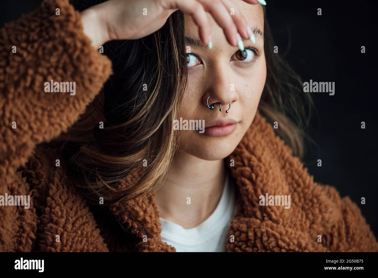 Eine junge, zufriedene, trendige Frau, die die Kamera anschaut, ist kreativ und hält ihre Hand schräg vor ihr Gesicht. Stockfoto
