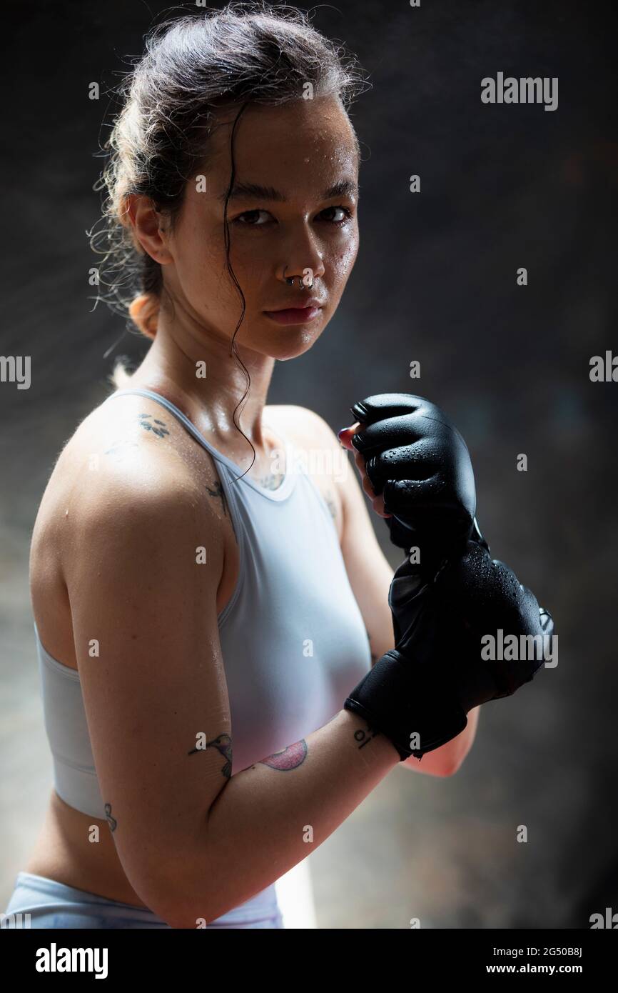Porträt einer jungen Frau, die Boxhandschuhe trägt und die Kamera anschaut. Sie hat ihre Fäuste auf und ist bereit zu kämpfen. Stockfoto