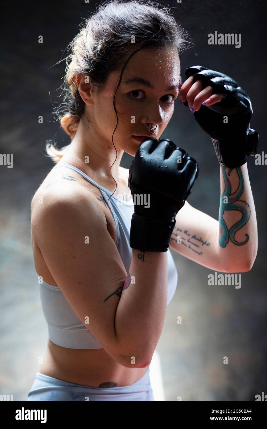 Porträt einer jungen Frau, die Boxhandschuhe trägt und die Kamera anschaut. Sie hat ihre Fäuste vor ihrem Gesicht und ist bereit zu kämpfen. Stockfoto