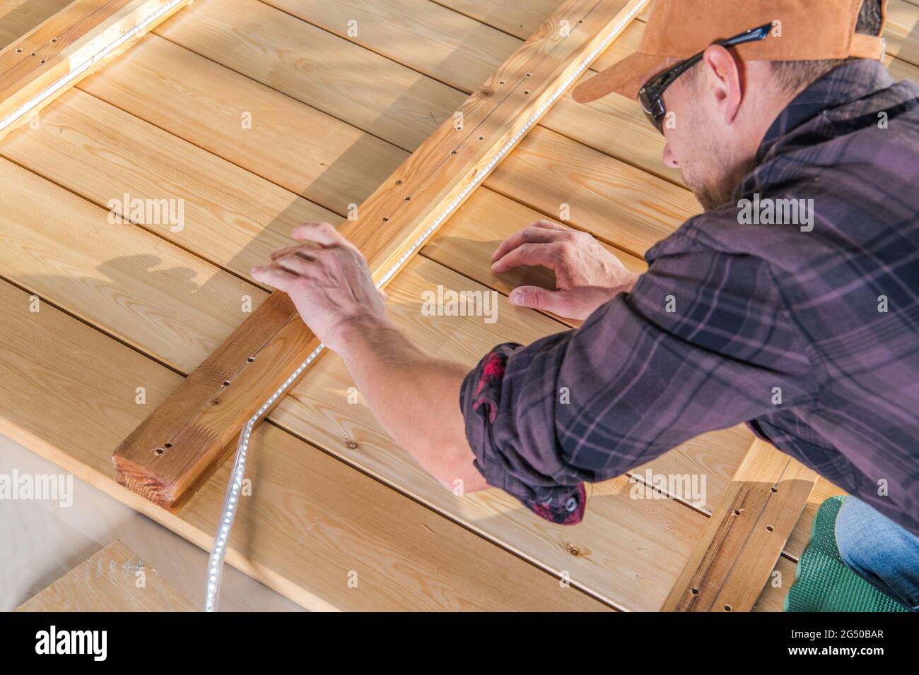 Arbeiter, der LED-Lichtband in Holzelementen des neu gebauten Decks installiert. Holzarbeiten. Stockfoto