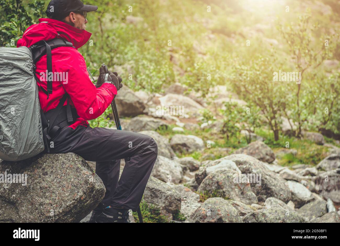 Kaukasischer Wanderer mit großem Rucksack, entspannender Sitzgelegenheit auf einem Felsblock. Thema Bergwanderung. Stockfoto